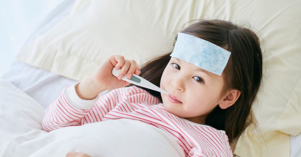 A young girl lays in bed with a thermometer in her mouth.