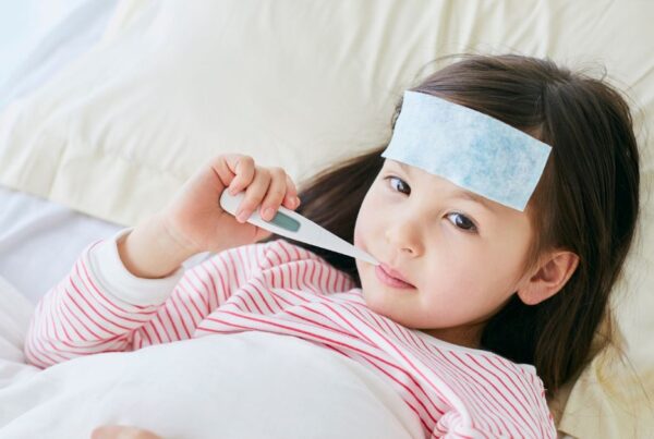 A young girl lays in bed with a thermometer in her mouth.