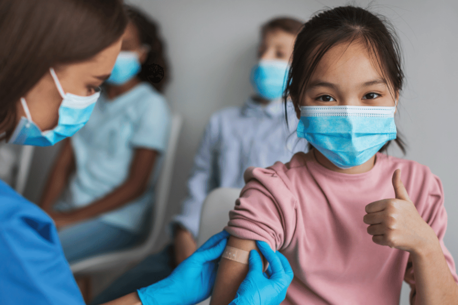 A child gets a bandaid post vaccination while other children wait in line.