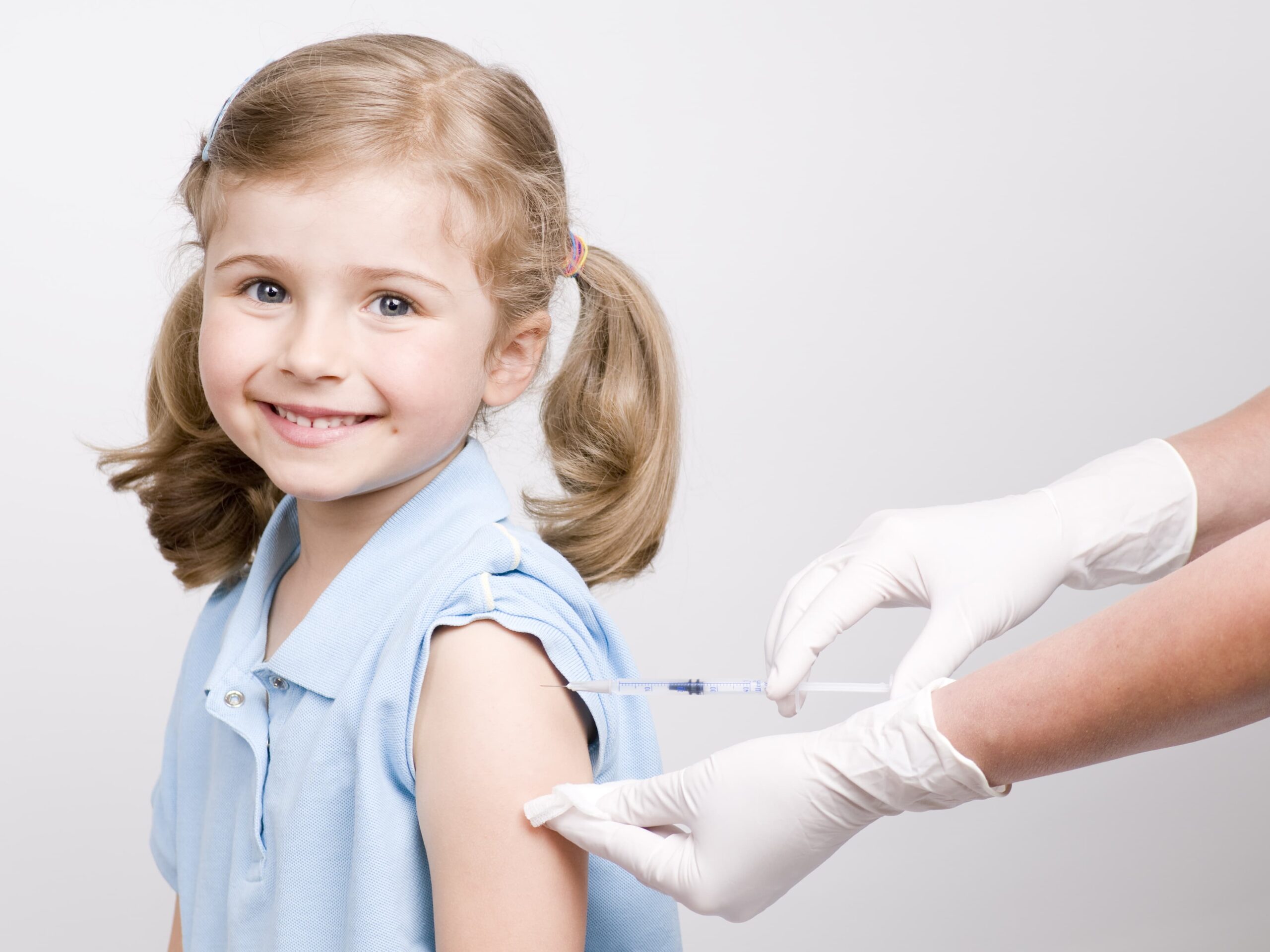 A smiling girl receives a vaccination in her arm.