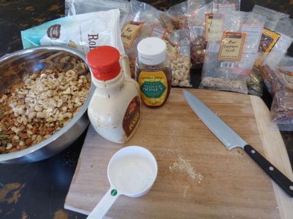 DIY granola ingredients, including a variety of nuts, honey, and maple syrup, lay on a kitchen counter.