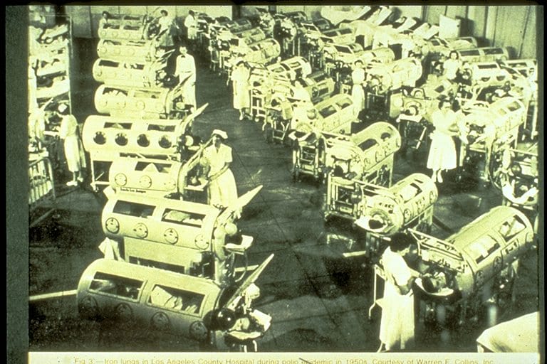 An old photograph of several polio patients in iron lungs. 