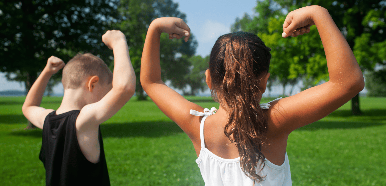 Two kids flex their arm muscles while they play outdoors.