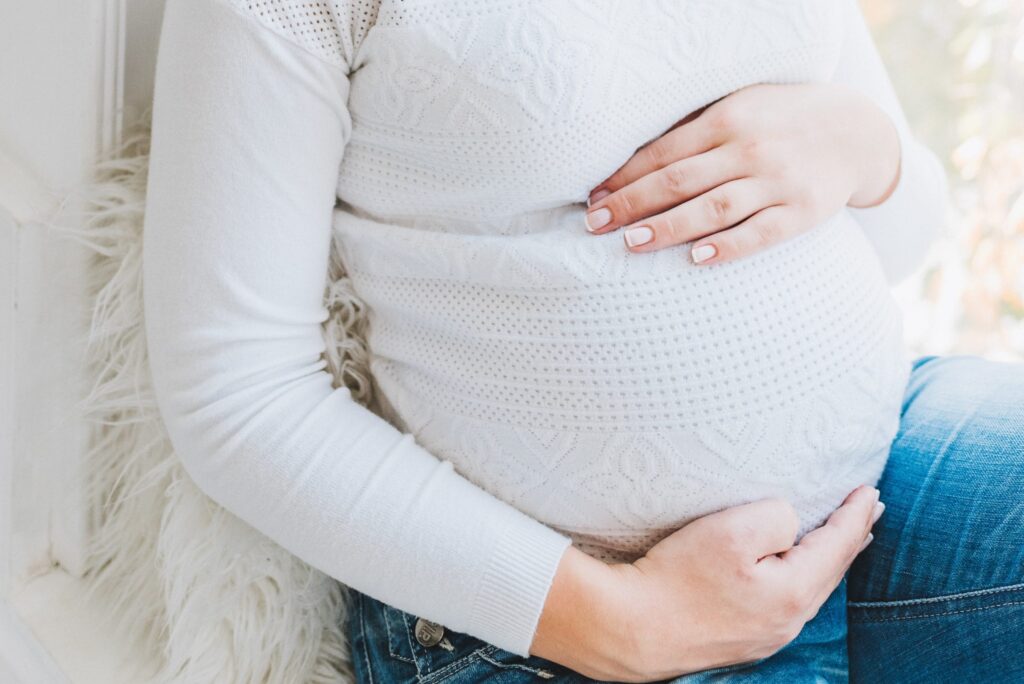 A close up photo of a pregnant woman's belly with her hands resting on her belly. 