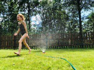 A girl runs through a sprinkler in her backyard. 