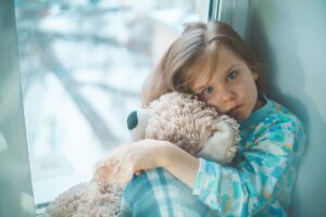 A sad young girl hugs her teddy bear.