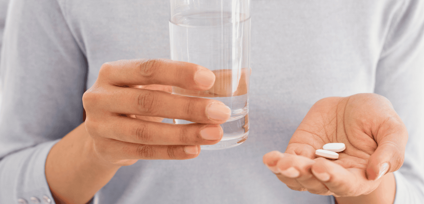 A person holding a glass of water and a couple of pain pills.