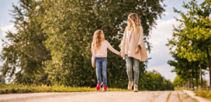 A mother and daughter hold hands as they take a walk outdoors together.