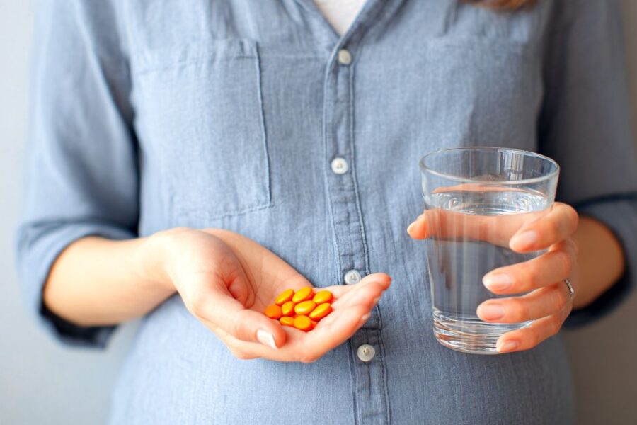 A woman holds pills and a glass of water in her hands.