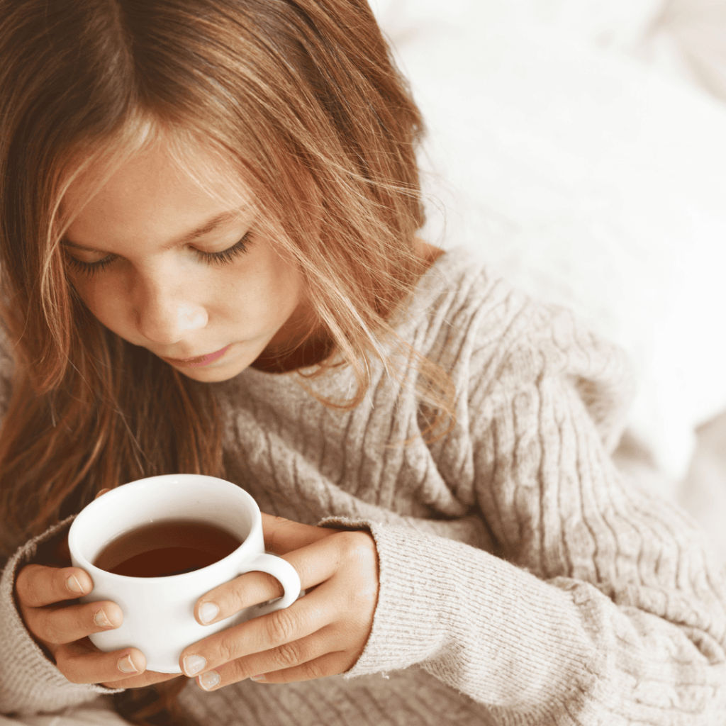 A girl holds a cup of herbal tea used to manage fevers. 