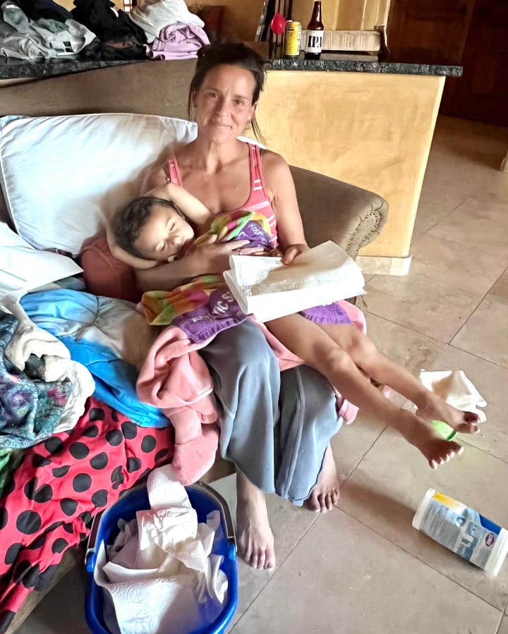 Dr. Green Mom (Ashley) holds her ailing son. A bucket, paper towels, and cleaning wipes surround them.