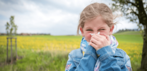 A girl blows her nose in a field blooming with yellow flowers.
