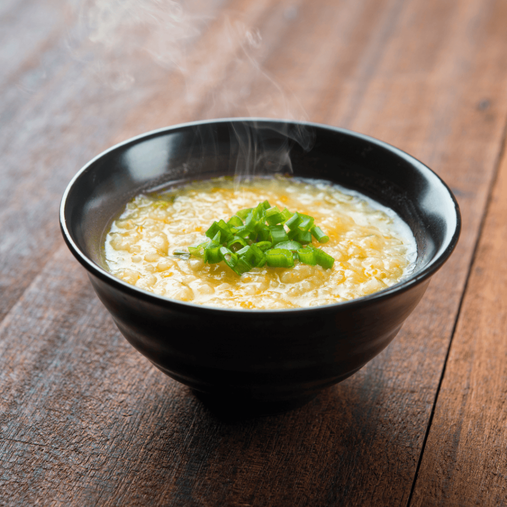 A steaming bowl of congee rests on a wooden table. 
