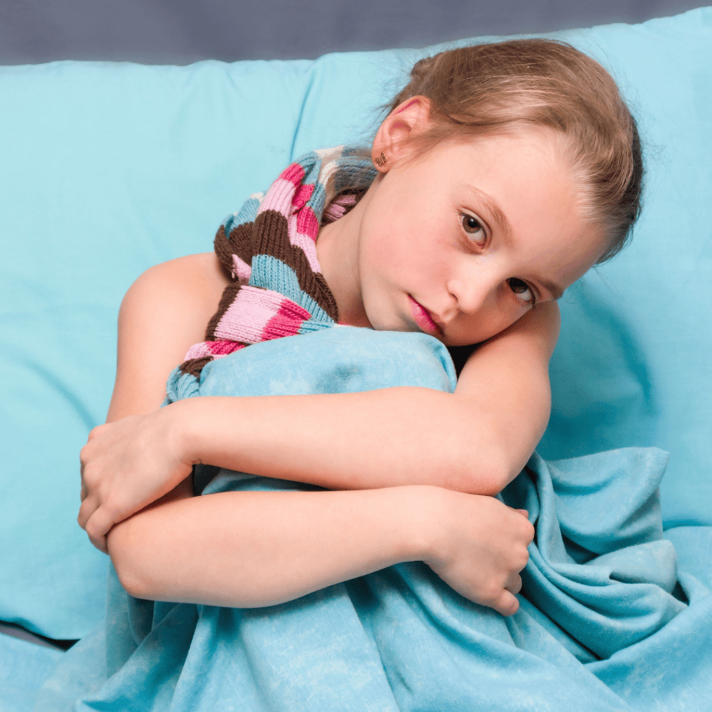 A forlorn child sits in bed hugging her knees to her chest.