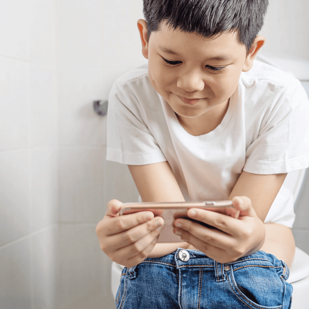 A boy plays on a cell phone while sitting on the toilet.
