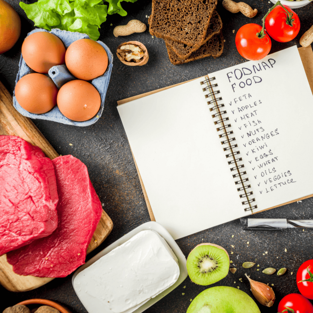 A notebook with a list of Fodmap foods lies open on a black counter surrounded by eggs, tomatoes, beef, kiwi, and tomatoes. 