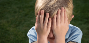 A young boy covers his eyes with his hands. (Pink Eye)