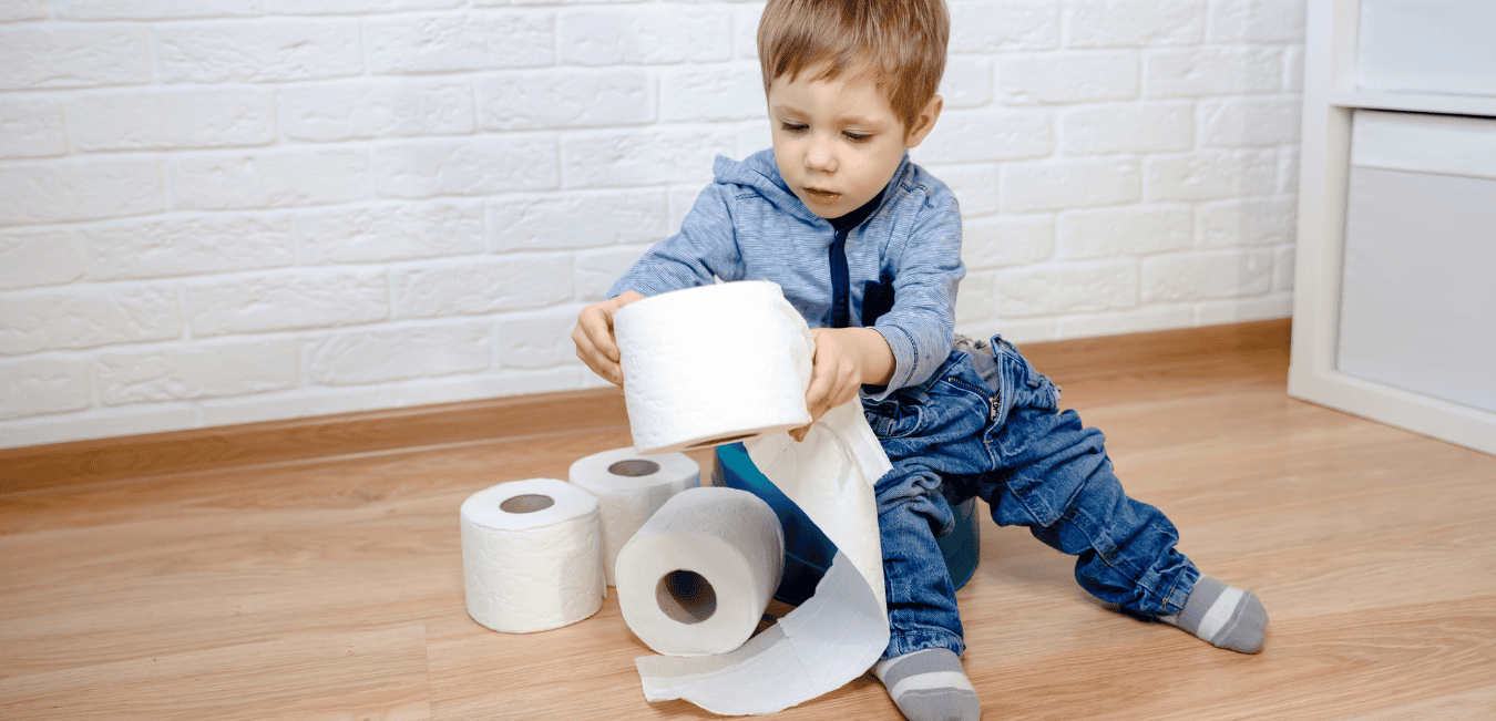 A young boy sits on the floor playing with four rolls of toilet paper.