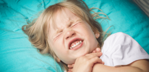 A young child in pain lies in bed gripping her throat.