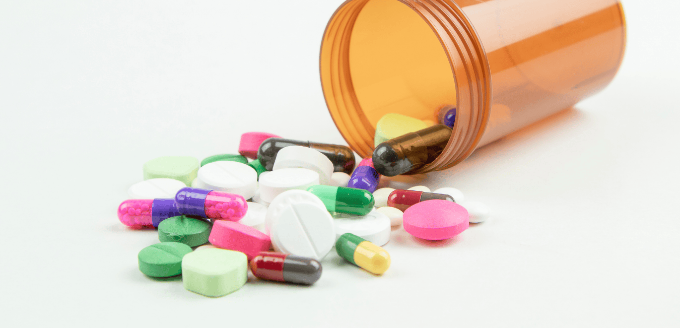 A brown medicine bottle tipped on its side with various colored pills spilled on the counter.