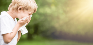 A boy standing in a green field coughs into his hands.