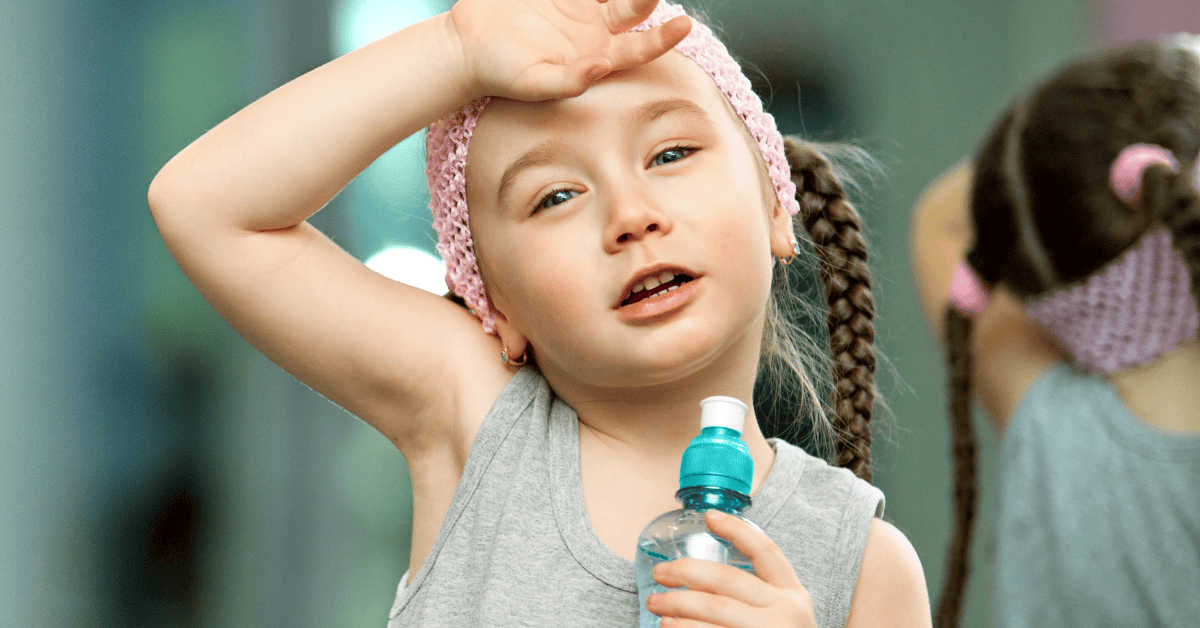 An overheated girl holds a hand to her forehead while holding a water bottle in her other hand.