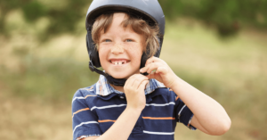A boy smiles as he buckles his black bicycle helmet under his chin.