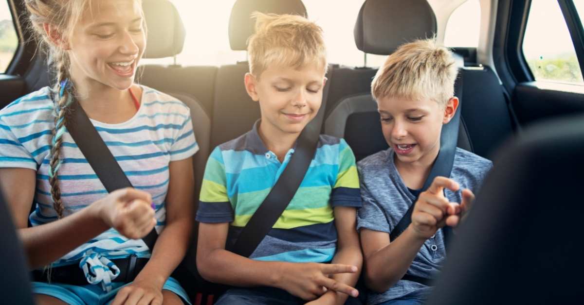 Three kids play in the backseat of a car while on a road trip.