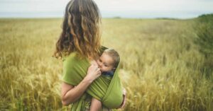 A mom stands in a field of tall green grass while breastfeeding her baby.