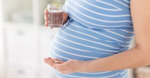 A pregnant woman holding a glass of water and vitamin in her hands.