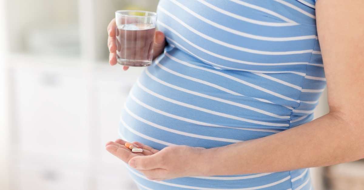A pregnant woman holding a glass of water and vitamin in her hands.