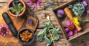 Colorful herbs neatly arranged on a round wooden cutting board and in a wooden basket set atop a wooden table.