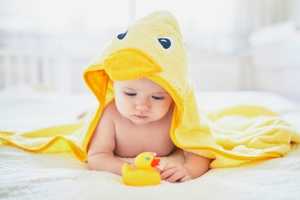 A baby wrapped in a yellow towel plays with a duck after his bath. 