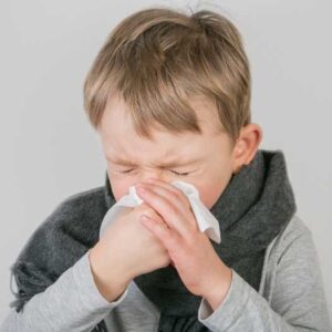 A young boy sneezing into a tissue. 