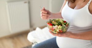 A pregnant woman eats a bowl of salad.