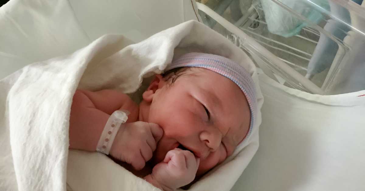 A newborn infant lies in a hospital bassinet.