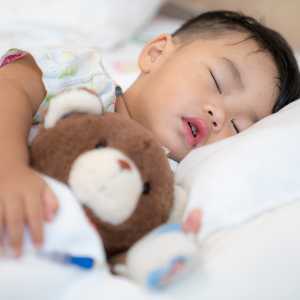 A boy holds his teddy bear while sleeping.