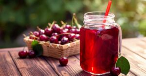 A glass of tart cherry juice sits on a wooden table in front of a basket of cherries.