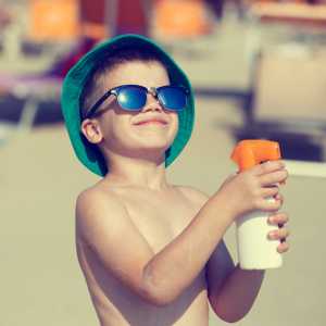 A boy at the beach sprays himself with after-sun spray.