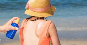 A parent sprays after-sun spray on a child's back.