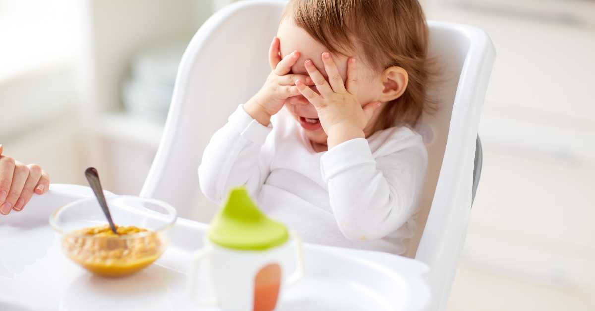 A frustrated toddler cries in her high chair.