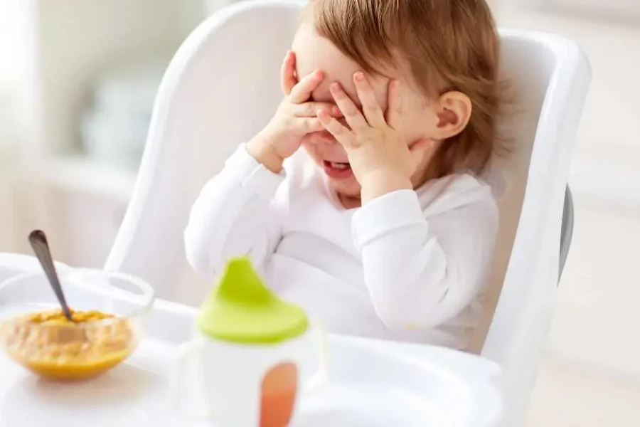 A frustrated toddler cries in her high chair.