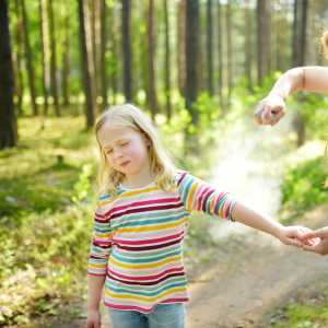A child walking in the woods is sprayed with insect repellent.