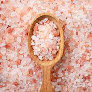 A wooden spoon dips into a large pile of pink Himalayan salt.