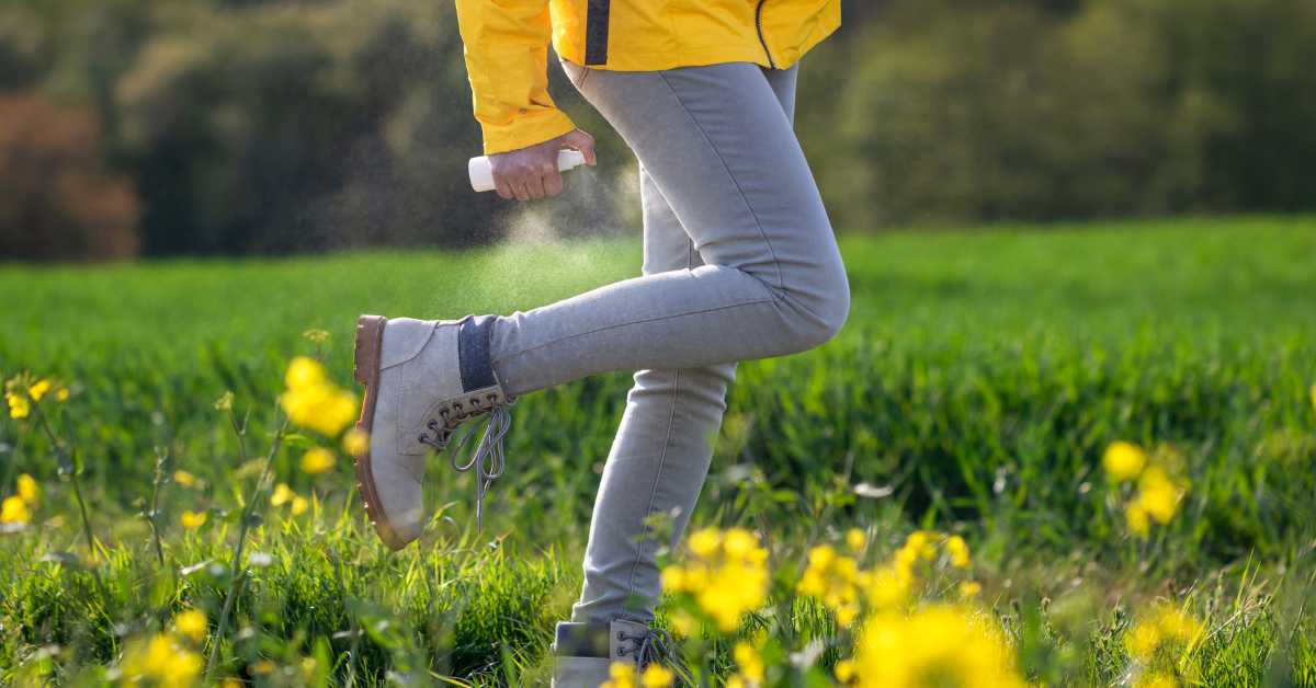 A woman sprays insect repellent on herself as she walks through a field.
