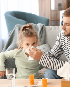 A sick girl blows into a tissue held by her father.