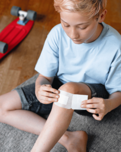 A boy applies a dressing to a wound on his knee. 