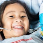 A young girl smiles while getting her teeth cleaned at the dentist.