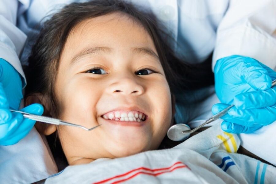 A young girl smiles while getting her teeth cleaned at the dentist.
