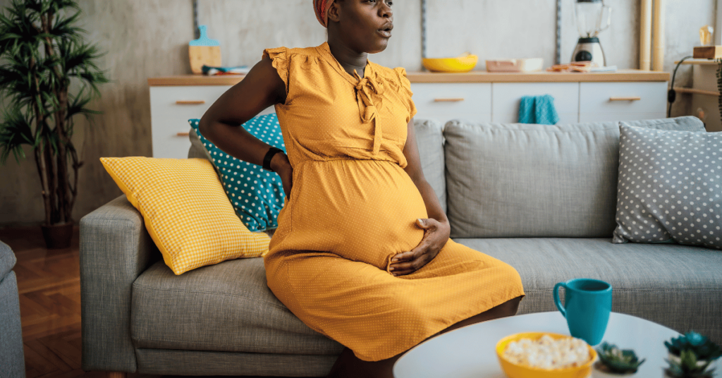 A pregnant woman in discomfort sits on a couch.
